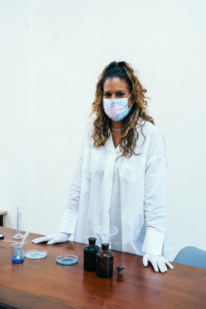 Female scientist in white coat conducting laboratory experiments with protective mask and gloves.